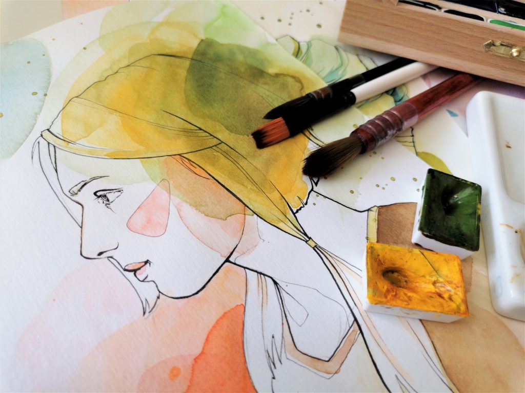 Paintbrushes and watercolour paints positioned on top of a portrait of a young woman.