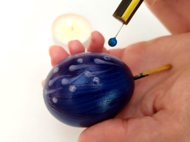 Hand holding a painted egg while applying further paint.