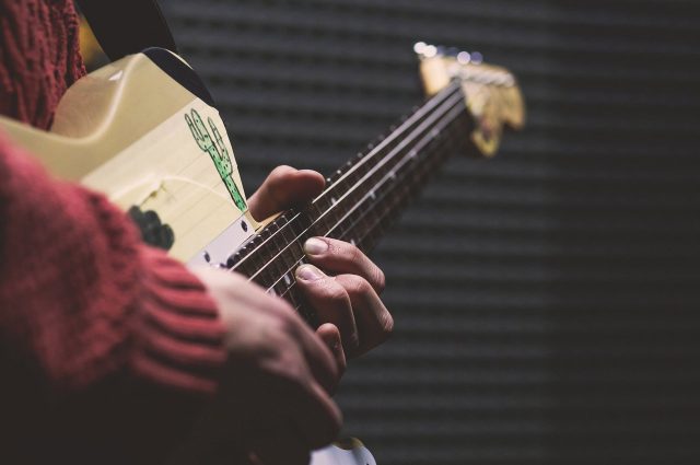 Close up images of a person holding a guitar with fingers on the strings.