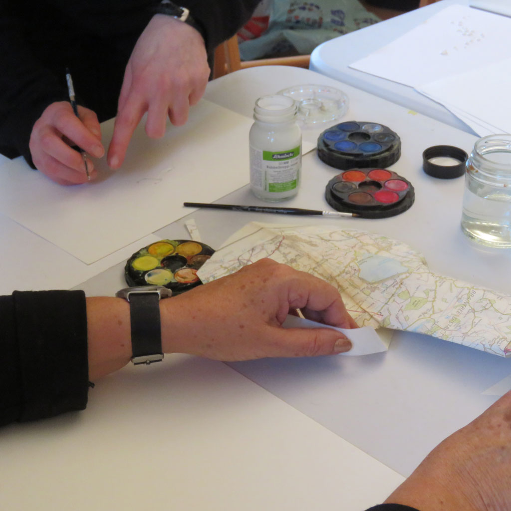 Close up of hands with watercolours, blank paper and a map.