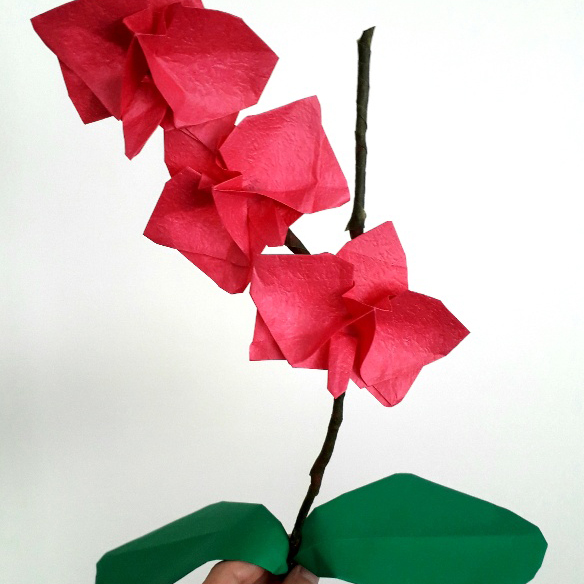 Pink paper flower on a stalk with two leaves.