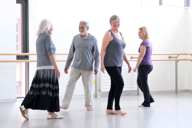 A man and three women wearing casual clothes standing in a dance studio smiling.