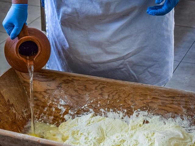 Person in blue gloves and an apron pouring water into a wooden tub of powder.