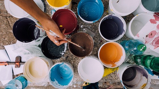 Ariel view of paint pots and a hand mixing one of the pots with a paintbrush.