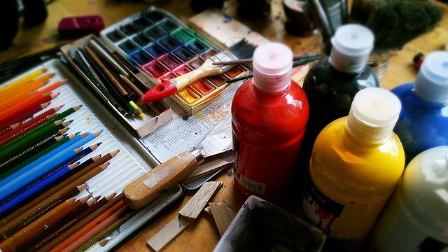 Bottles of paint, a watercolour paint set, brushes and coloured pencils.